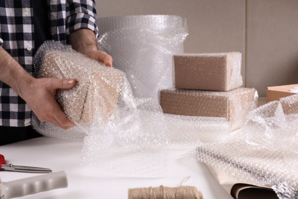 Man positioned at a packing station, wrapping cardboard boxes in bubble wrap